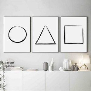 May include: Three black and white minimalist art prints featuring a circle, triangle, and square on a white background. The prints are framed in black and hung on a white wall.