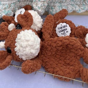 May include: A brown and white crocheted Highland snuggler toy with a price tag that reads "Highland Snuggler $15.00".