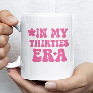 May include: White ceramic mug with a pink design that says "*IN MY THIRTIES ERA" with a star on either side of the text.