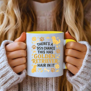 Op de afbeelding: Witte keramische mok met een gele binnenkant en handvat. De mok heeft de tekst "THERE'S A 95% CHANCE THIS HAS GOLDEN RETRIEVER HAIR IN IT" in goud en bruin, samen met pootafdrukken, honden silhouetten en tennisballen.