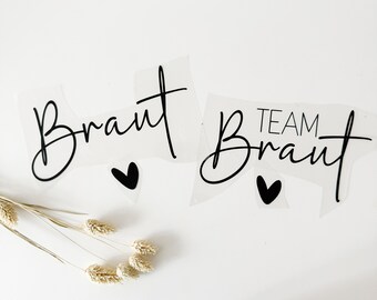 May include: Two white vinyl stickers with black lettering. The first sticker says "Braut" with a small black heart below it. The second sticker says "Team Braut" with a small black heart below it.