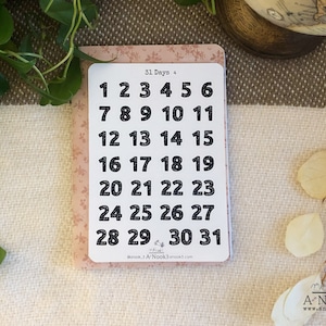 May include: A sheet of 31 black and white number stickers on a pink background. The numbers are in a bold font and range from 1 to 31. The text "31 Days +" is at the top of the sheet.