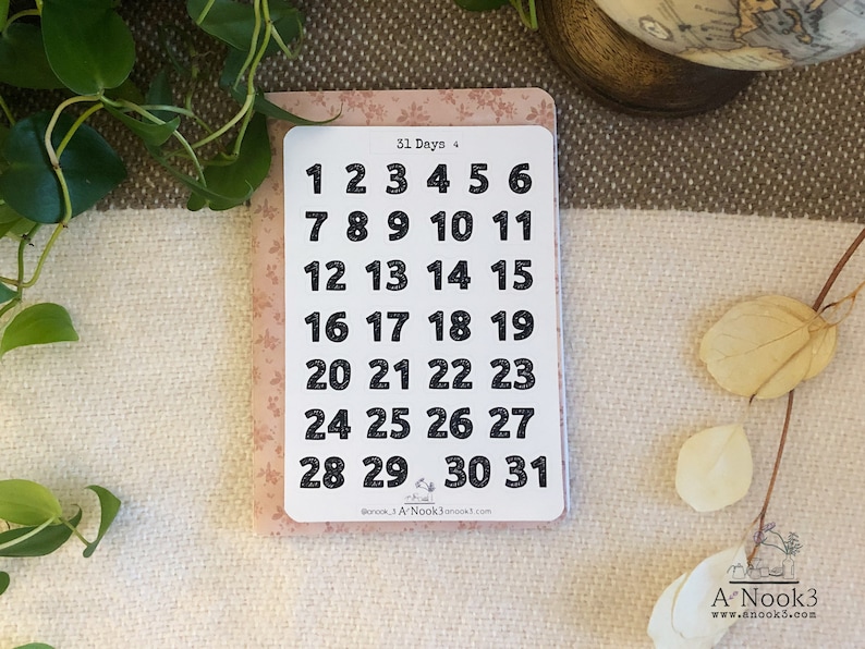 May include: A sheet of 31 black and white number stickers on a pink background. The numbers are in a bold font and range from 1 to 31. The text "31 Days +" is at the top of the sheet.