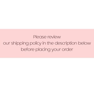May include: A rectangular graphic with a light pink background featuring dark brown text that reads: Please review our shipping policy in the description below before placing your order. The text is centered and written in a simple sans-serif font.