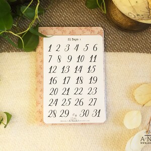 May include: A pink card with a floral pattern and the text "31 Days 1" printed on it. The card has a list of numbers from 1 to 31 in black ink.