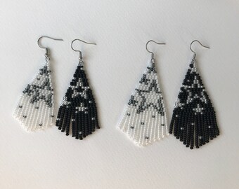 May include: A pair of black and white beaded earrings with a star pattern. The earrings are teardrop shaped and have a fringe at the bottom.