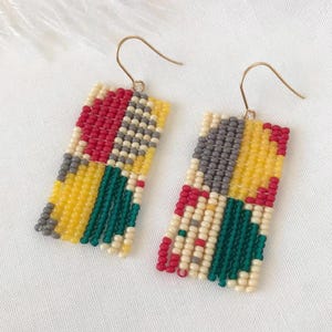 May include: A pair of colorful beaded earrings with a geometric pattern in shades of red, yellow, green, gray, and white. The earrings are made with small beads and have a gold hook.