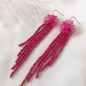 Op de afbeelding: Roze bloem oorhangers met een kralen franje. De oorhangers zijn gemaakt van kleine roze kralen en hebben een gouden haak.