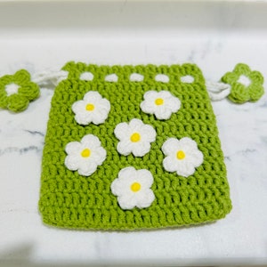 May include: A green crocheted drawstring bag with white daisy flowers. The bag has a white crocheted flower on each side.