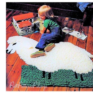 May include: A child sits on a white fluffy sheep rug with a green grass base. The rug is shaped like a sheep with a head and legs. The child is wearing blue jeans and a green shirt.