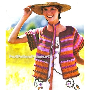 Peut inclure: Un gilet en crochet avec un motif rayé orange, rose et violet. Le gilet a une fermeture à nouer et un pompon. Le gilet est porté sur une robe blanche à broderies florales.