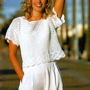 May include: A white crochet top with a scoop neck and short sleeves. The top is made with a delicate open stitch pattern.