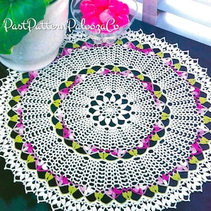 May include: White crochet doily with a green and pink floral design. The doily is laid out on a dark blue surface.  PastPatternPaboozaCo is printed on the image.