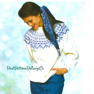 May include: White knitted sweater with a blue and white geometric pattern around the neckline. The sweater has long sleeves and a relaxed fit. The model is wearing a blue scarf and a denim skirt.