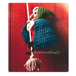May include: A crocheted witch doll with a green hat and blue robe holding a broom. The doll is hanging on a red wooden door. The text "PastPatternPaloozaCo" is visible in the bottom right corner of the image.