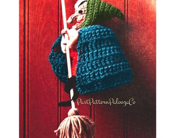May include: A crocheted witch doll with a green hat and blue robe holding a broom. The doll is hanging on a red wooden door. The text "PastPatternPaloozaCo" is visible in the bottom right corner of the image.