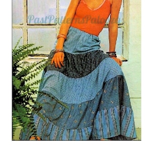 Op de afbeelding: Een vrouw draagt een oranje top zonder mouwen en een lange, blauwe en witte gelaagde rok. Ze zit op een vensterbank met een varenplant op de voorgrond.