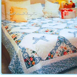 Może przedstawiać: Łóżko pokryte jest kwiecistą kołdrą i kilkoma białymi poduszkami. Kołdra ma białe tło z niebieskimi geometrycznymi wzorami i kwiatowymi akcentami. Mała, brzoskwiniowa poduszka znajduje się na środku. Widoczny jest tekst "Past Pattern Palooza Co".