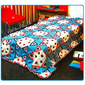 May include: A colorful, handmade crochet blanket. The blanket features a geometric pattern with blue, white, and red squares and triangles. The edges are finished with a red border. The blanket is displayed on a bed.