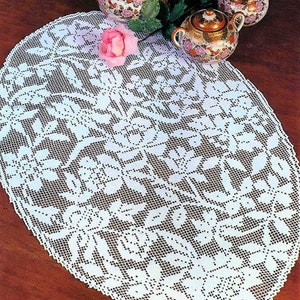 Puede incluir: Mantel ovalado de ganchillo blanco con un diseño floral. El mantel está sobre una mesa de madera con tres tazas de té de porcelana y una tetera con motivos florales.