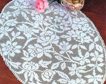 May include: White crocheted oval tablecloth with a floral design. The tablecloth is on a wooden table with three porcelain teacups and a teapot with floral patterns.