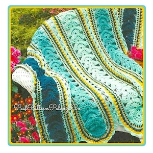 Może przedstawiać: Ręcznie robiony koc z dzianiny w kolorze turkusowym, niebieskim, żółtym i zielonym. Koc ma falowany brzeg i powtarzający się wzór owali.