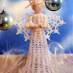 May include: A crocheted angel ornament with a white lace dress and a halo. The angel is standing on a wooden surface with white feathers in the background.