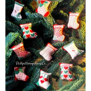 May include: Twelve small, hand-stitched Christmas stockings with various designs, including hearts, reindeer, and plaid patterns. The stockings are hung on a green pine tree branch.