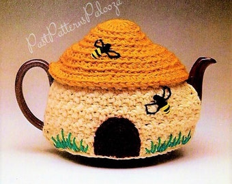 May include: A crocheted teapot cosy shaped like a beehive with a brown door and green grass. Two yellow and black bees are embroidered on the cosy.