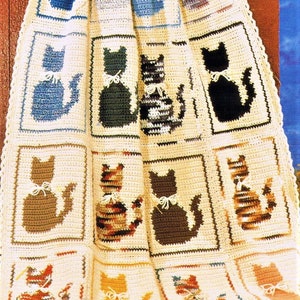 May include: A crocheted blanket featuring a pattern of cats in various colours. The blanket is made from beige yarn and showcases a range of cat designs, including black, brown, blue, and orange.