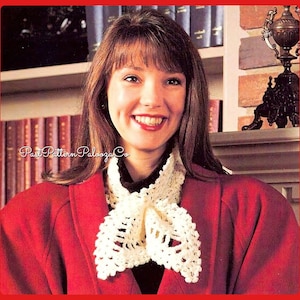 May include: A woman wearing a red jacket with a white crocheted collar. The collar is tied in a bow at the front. The woman is smiling and looking at the camera.