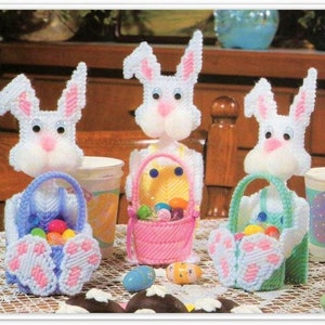 May include: Three white crocheted Easter bunny baskets with pink, blue, and green accents. Each bunny is holding a basket filled with colorful candy eggs.
