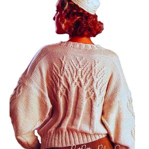 May include: Cream-colored, oversized knit sweater with a textured leaf design on the back. The sweater has long sleeves and a ribbed hem. A matching knit hat is also visible. The image is from PastPatternPaloozaCo.