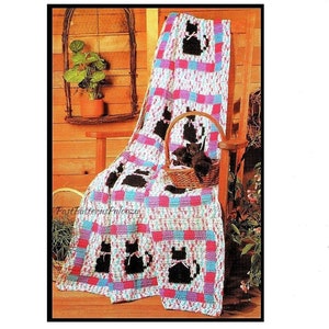 Puede incluir: Una manta de crochet con un diseño de gato negro en un patrón de patchwork de rosa, azul y blanco. La manta está drapeada sobre una silla de madera.