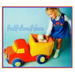May include: A plush toy truck featuring a red cab with orange patterned accents, a yellow cargo bed, and blue wheels with yellow centres. A small white plush animal sits inside the cargo bed. The text PastPatternsPalooza is visible.