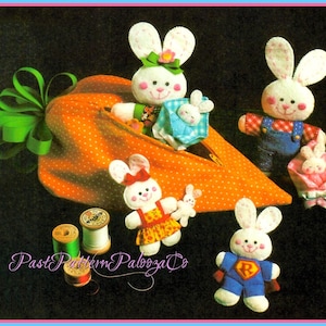 May include: A set of four felt bunny rabbit toys in a carrot-shaped fabric pouch. The bunnies are dressed in different outfits, including a blue and white dress, a red and blue superhero costume, a red and white gingham dress, and a blue and white overalls. The pouch is orange with white polka dots and has a green ribbon.