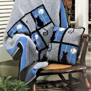 May include: A crocheted throw blanket and pillow featuring a black cat silhouette design with a moon and stars. The blanket and pillow are in shades of blue, gray, and white.