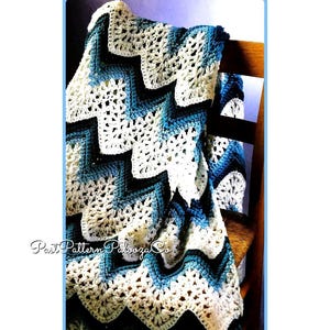 May include: A crocheted chevron blanket in shades of blue and white, draped over a wooden chair. The blanket features a repeating chevron pattern and a delicate crocheted border.