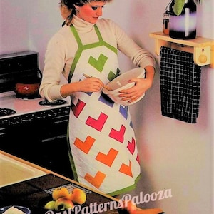 Op de afbeelding: Een vrouw in een wit shirt en een kleurrijk patchwork-schort mengt beslag in een witte kom. Ze staat in een keuken met een fornuis en een houten plank met een handdoek eraan. Er liggen appels en een deegroller op het aanrecht.