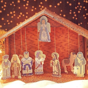 May include: A wooden nativity scene with a brown roof and a brick-like wall.  The scene features a hanging angel, a donkey, a shepherd, and three wise men.  The figures are made of beads and are hanging from strings.
