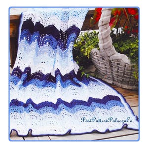 May include: A crocheted blanket in white, light blue, and navy blue, with a scalloped edge. The blanket is draped over a wooden surface, with a basket and greenery in the background. The text "PastPatternPaloozaCo." is visible.