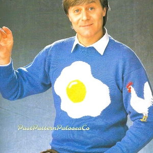 May include: A blue knitted sweater with a white and yellow fried egg design and a white rooster on the right sleeve. The text "PastPatternPaloozaCo" is printed on the sweater.