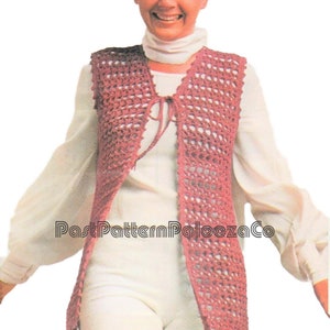 Può includere: Un gilet di uncinetto con chiusura a cravatta. Il gilet è di colore rosa chiaro e presenta un motivo a pizzo. Il gilet è indossato da una donna con capelli corti castani.