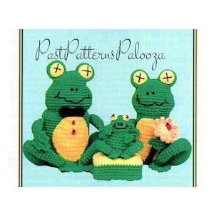 May include: Crochet pattern for a family of three frogs. The frogs are green with yellow bellies and have black eyes with white crosses. The pattern includes instructions for making a flower.