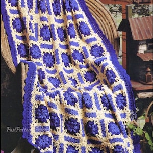 May include: A crocheted blanket with a blue and yellow checkered pattern. The blanket is made of squares with a flower design in the center. The blanket is draped over a wicker chair.