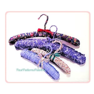 May include: Four fabric-covered padded clothes hangers featuring various patterns including dark floral, purple floral, light floral, and blue gingham check. Each hanger includes a fabric-wrapped hook and a small decorative bow. Text reads PastPatternsPalooza.