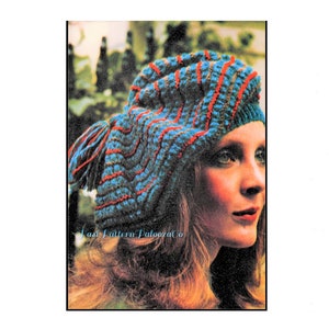 May include: A blue and red striped crocheted beret with a small tassel. The beret is worn by a woman with long brown hair.