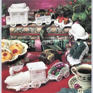 Peut inclure: Un ensemble de décorations de train de Noël en crochet blanc. Le train comprend une locomotive, un wagon de passagers, un wagon avec un sapin de Noël, un wagon avec des boules et un wagon avec des bâtonnets de cannelle. Les décorations sont présentées sur une nappe rouge et blanche avec des cadeaux emballés et une assiette de biscuits.