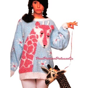 May include: A blue and pink knitted sweater with a giraffe design. The sweater has a white trim and a fluffy texture. The model is wearing a black hat and white leggings.