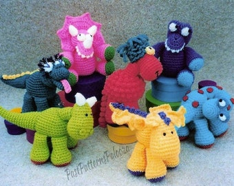 Puede incluir: Siete juguetes de dinosaurio de crochet en varios colores, incluyendo verde, rosa, morado, azul y amarillo. Los dinosaurios están sentados en cajas de colores.